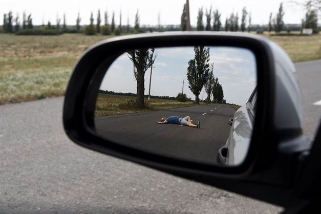 Side view mirror shows a person lying on a road. The image relates to leaving the scene of an accident.